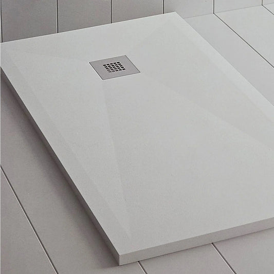 alt='Pormenor da base de chuveiro MEVA branca com textura ardósia e grelha de escoamento central.'