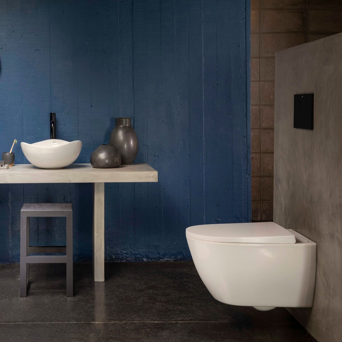 Vista lateral de sanita suspensa com tampo Roca Ona extrafino num ambiente de casa de banho com parede azul e lavatório de pousar.