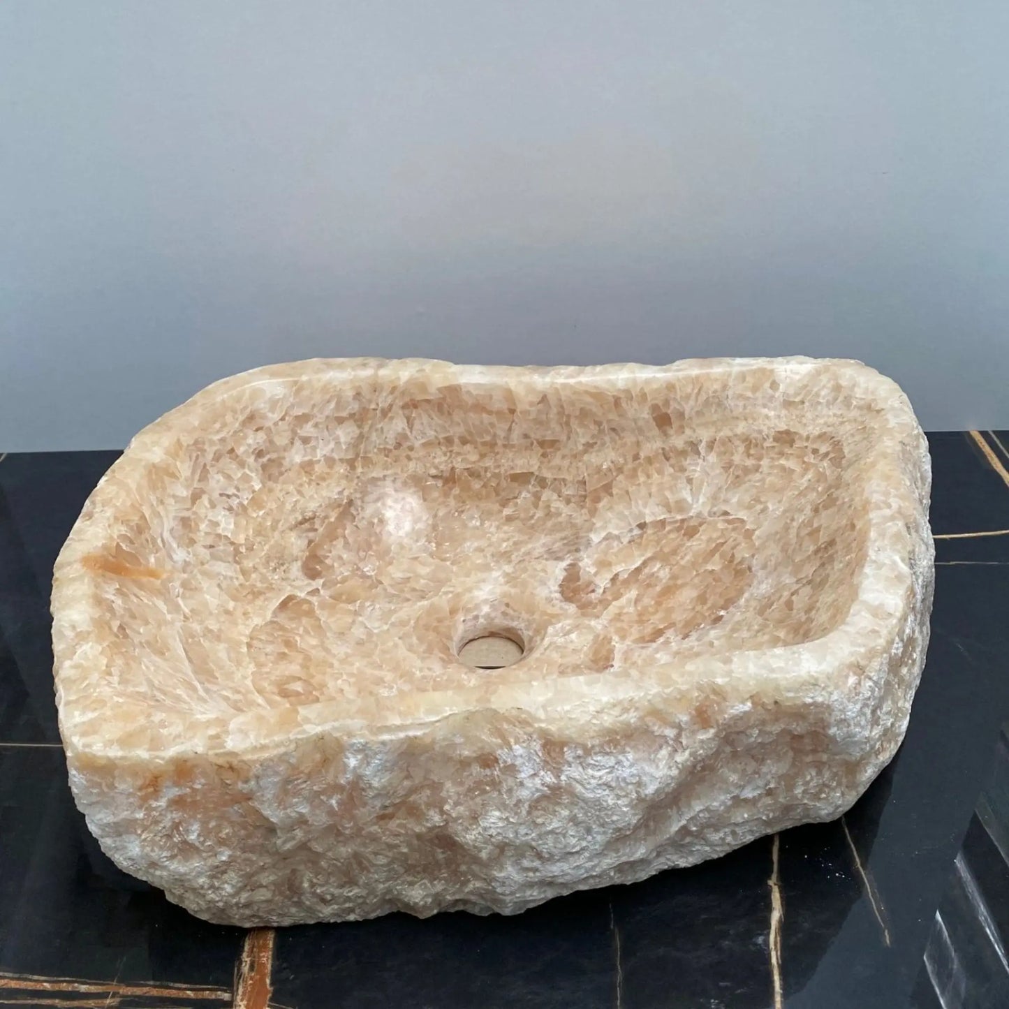 Lavatório de pousar retangular Fosil Onix 13 em pedra natural com exterior rustico, assente numa bancada preta.