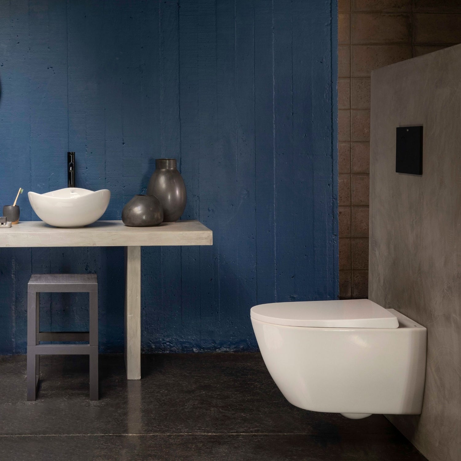 Vista lateral de sanita suspensa com tampo Roca Ona extrafino num ambiente de casa de banho com parede azul e lavatório de pousar.