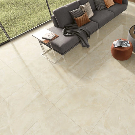alt='Pavimento cerâmico Marble Cream polido aplicado numa sala de estar moderna com um sofá cinzento e ampla janela.'