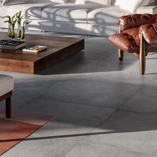 Alt text: 'Pavimento cerâmico ON-ROAD Antracite 30x60cm numa sala de estar com sofá cinza e poltrona de couro marrom.'