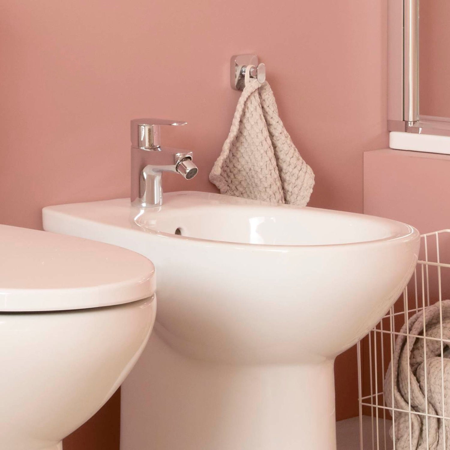 Torneira de bidé Roca Victoria Plus cromada instalada num bidé branco, em casa de banho de parede rosa.