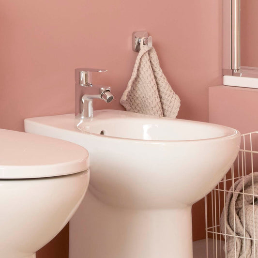 Torneira de bidé Roca Victoria Plus cromada instalada num bidé branco, em casa de banho de parede rosa.