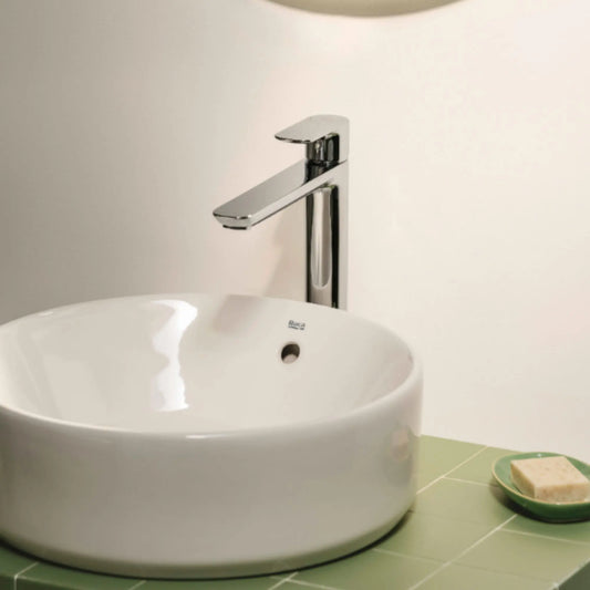 alt='Torneira de cano alto Roca Cala cromada, instalada numa bancada verde com um lavatório de pousar redondo.'